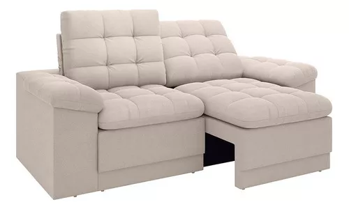Sofá secional bege com chaise longue. As almofadas e o encosto apresentam detalhes tufados, criando um padrão de grade. Os apoios de braço são acolchoados, aumentando o conforto geral e o apelo visual. O sofá tem um design moderno e minimalista, adequado para um espaço de estar contemporâneo.